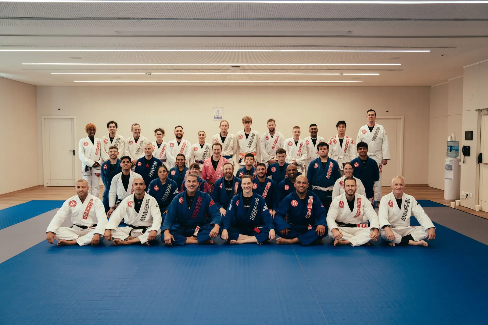 A large group of Gracie Barra students seated and standing on academy mats